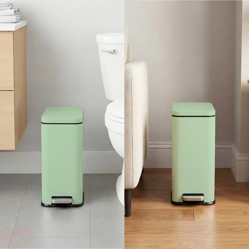 iTouchless green step trash can in a bathroom setting with a toilet in the background and living room between couch and wall.